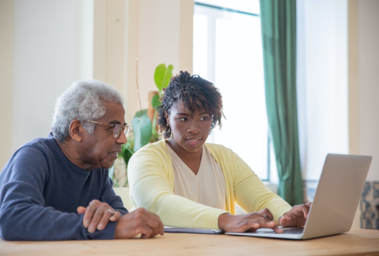 elderly man sitting with younger woman looking at laptop